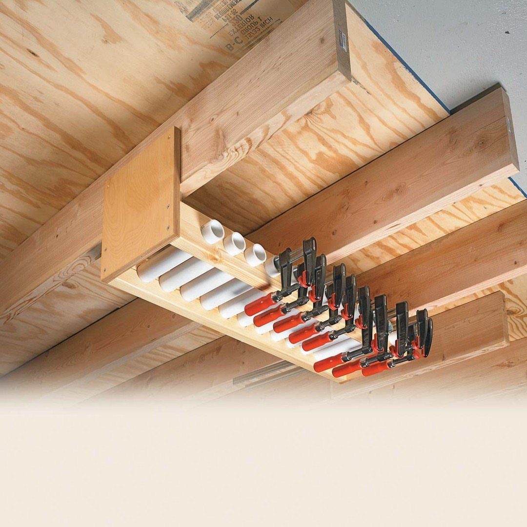 Wooden rack with PVC pipes holding red and black clamps under ceiling joists