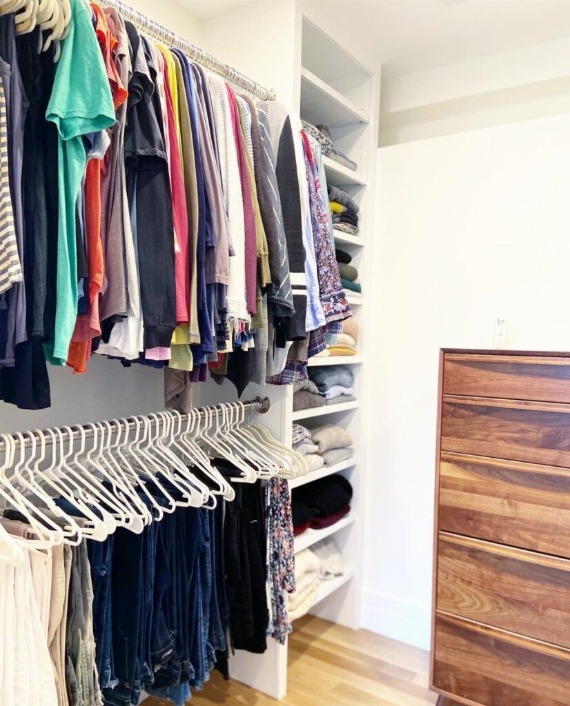 Two hanging rods at different levels holding shirts and jeans in a closet.