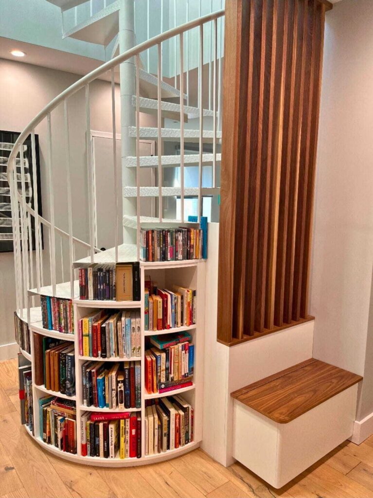 White curved staircase with integrated bookshelves filled with colorful books and wooden flooring.