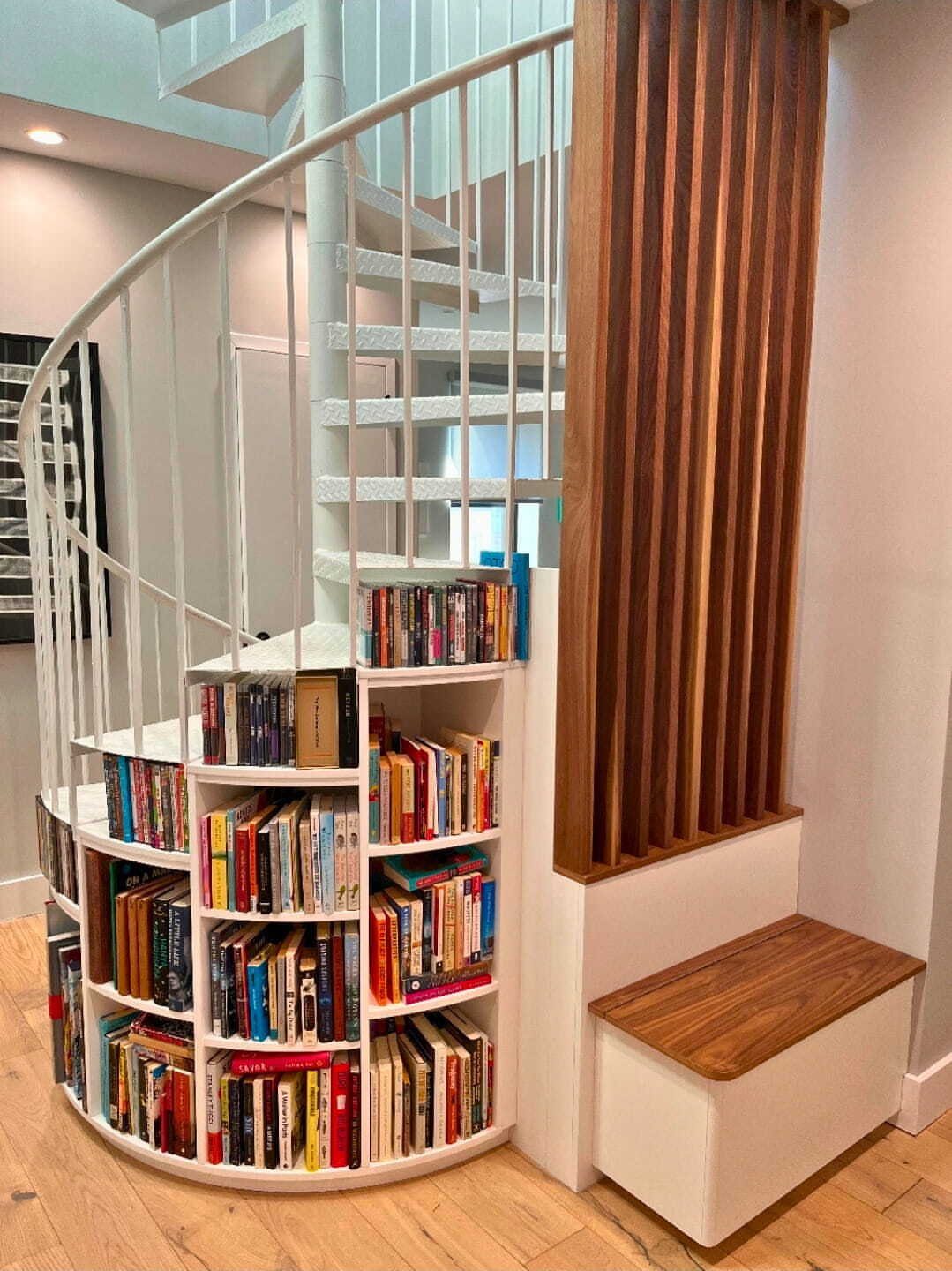 White curved staircase with integrated bookshelves filled with colorful books and wooden flooring.