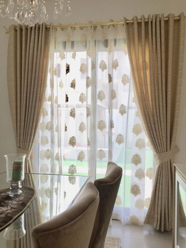 Double curtains with beige drapes and gold patterned sheers in a living room.