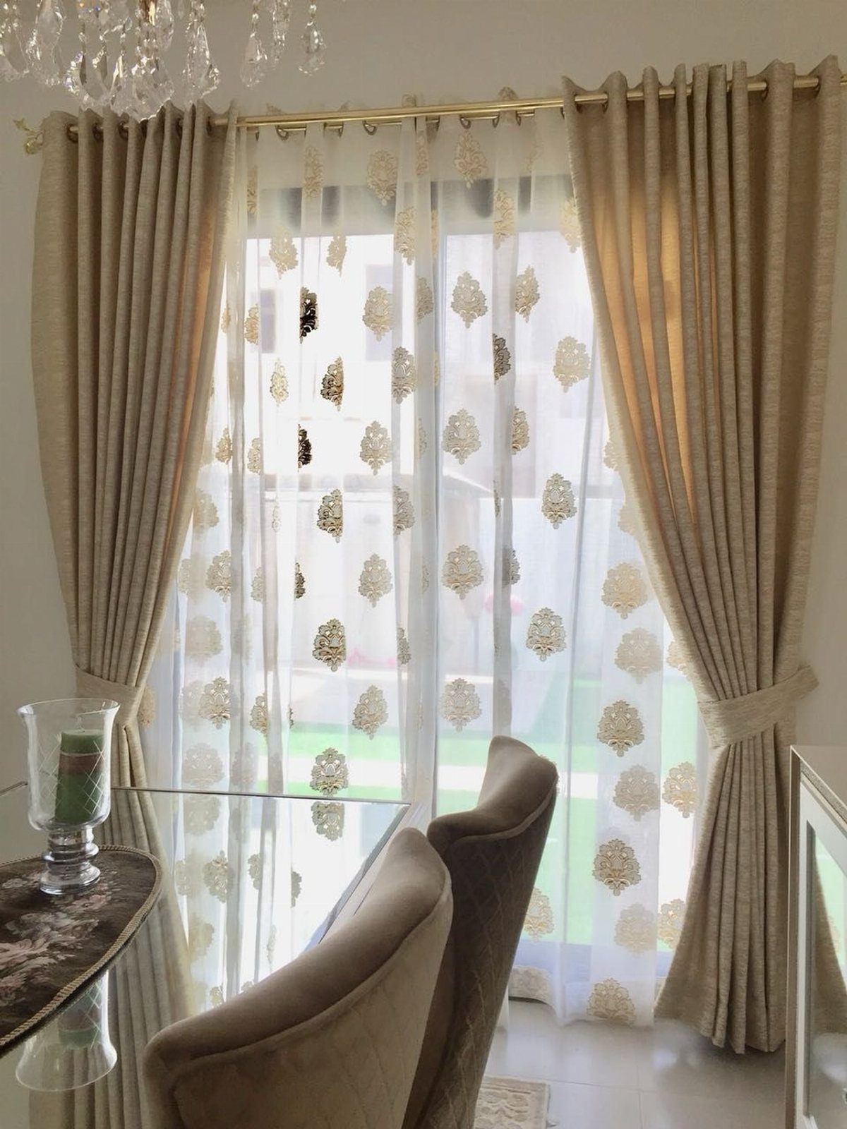Double curtains with beige drapes and gold patterned sheers in a living room.
