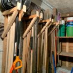 Wooden wall rack organizing various long-handled garden tools and shovels in a shed.