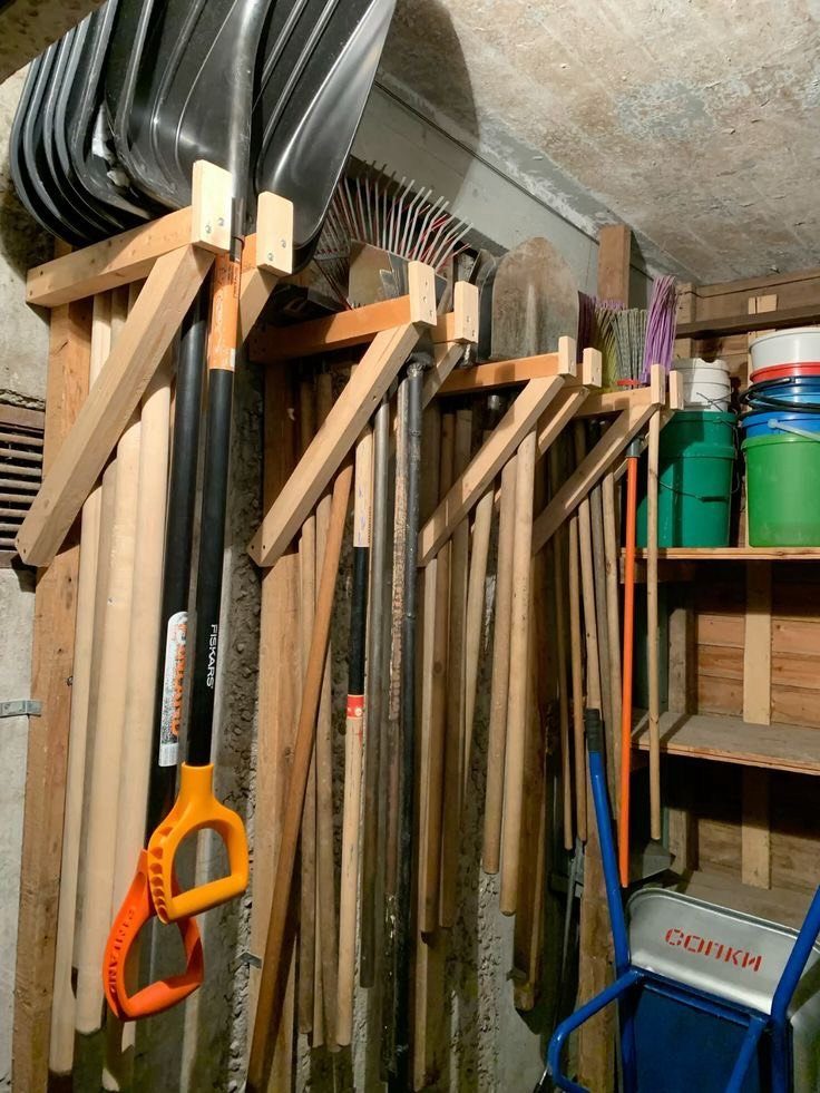 Wooden wall rack organizing various long-handled garden tools and shovels in a shed.