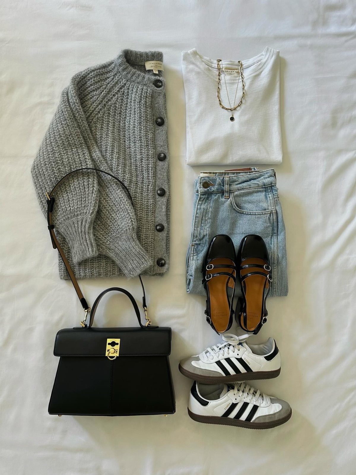 Grey cardigan, white t-shirt, blue jeans, sneakers, sandals, and black handbag on white fabric.