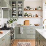 Sage green kitchen storage cabinets with doors and gold hardware in a bright kitchen.