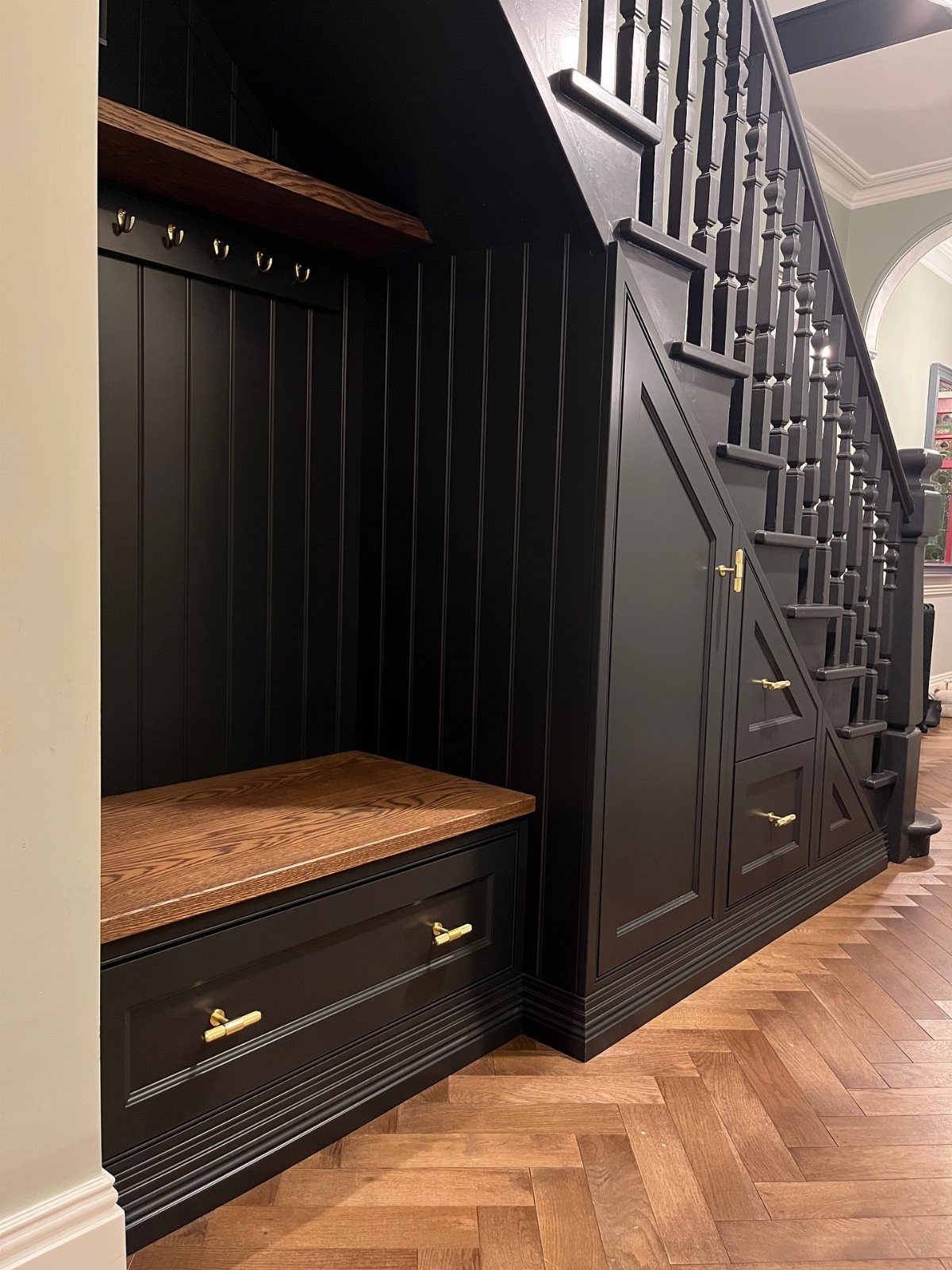 Black built-in mudroom with wooden bench and storage cabinets under a staircase.
