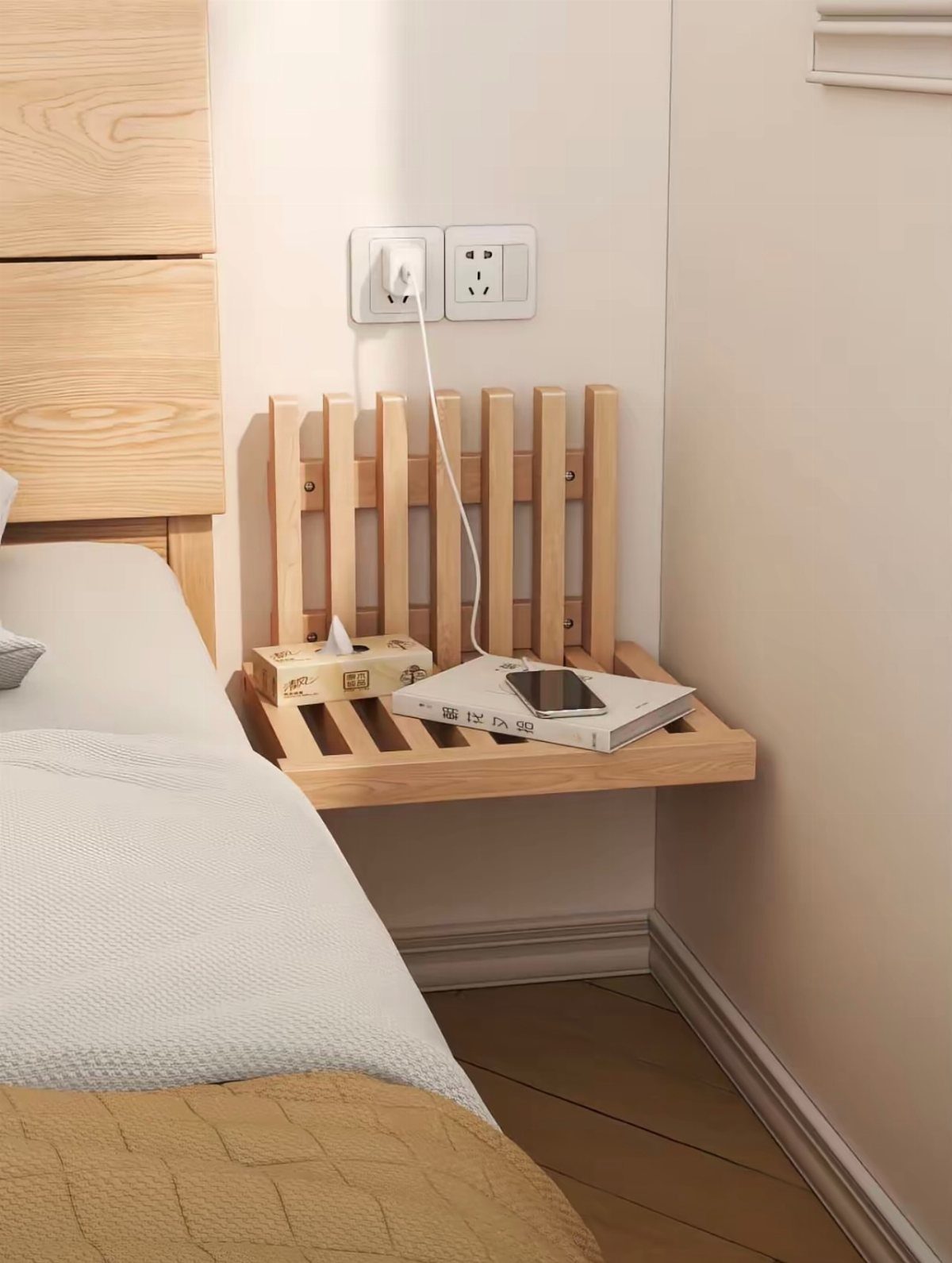 Wooden floating nightstand with a smartphone and tissues next to a bed.