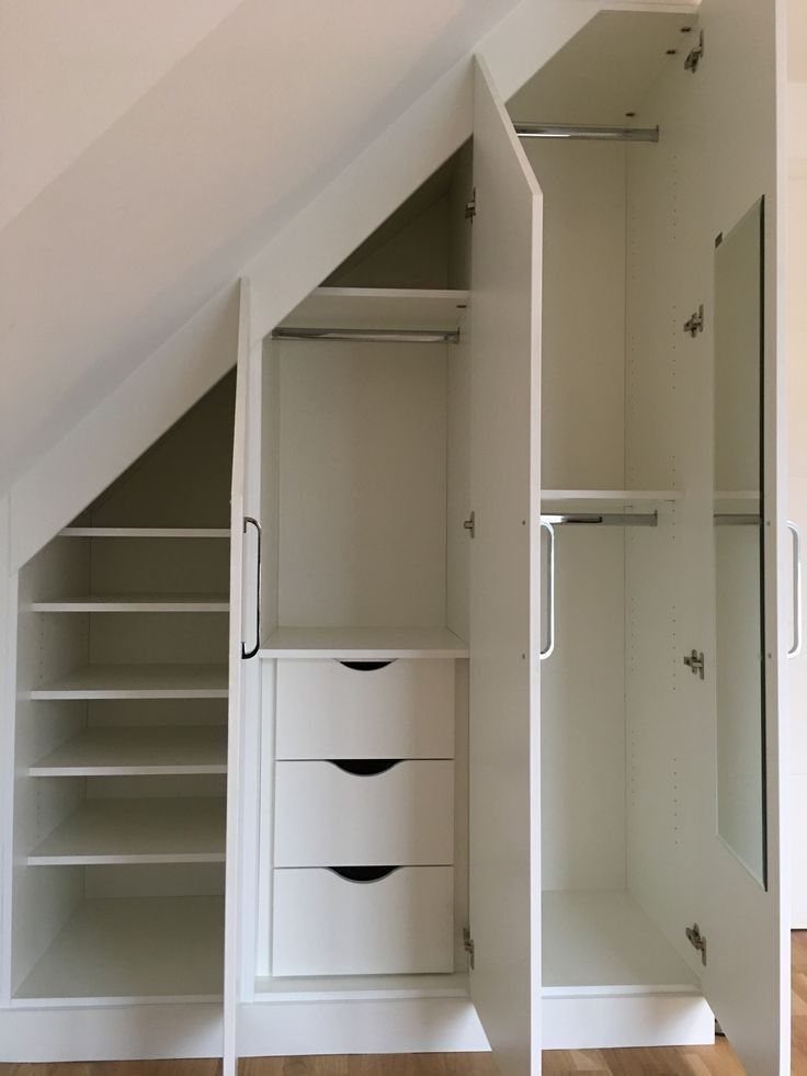 White built-in wardrobes under a sloped ceiling with shelving, drawers, and a full-length mirror.
