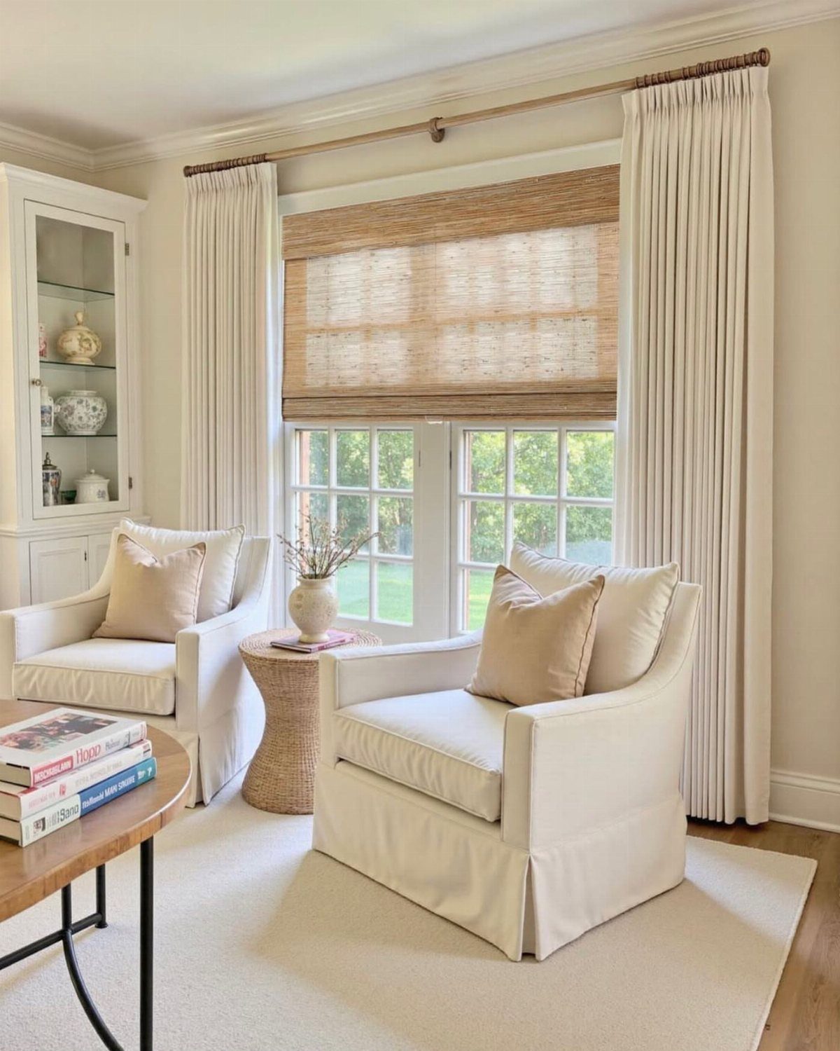 White curtains and a bamboo shade framing a window in a bright living room.